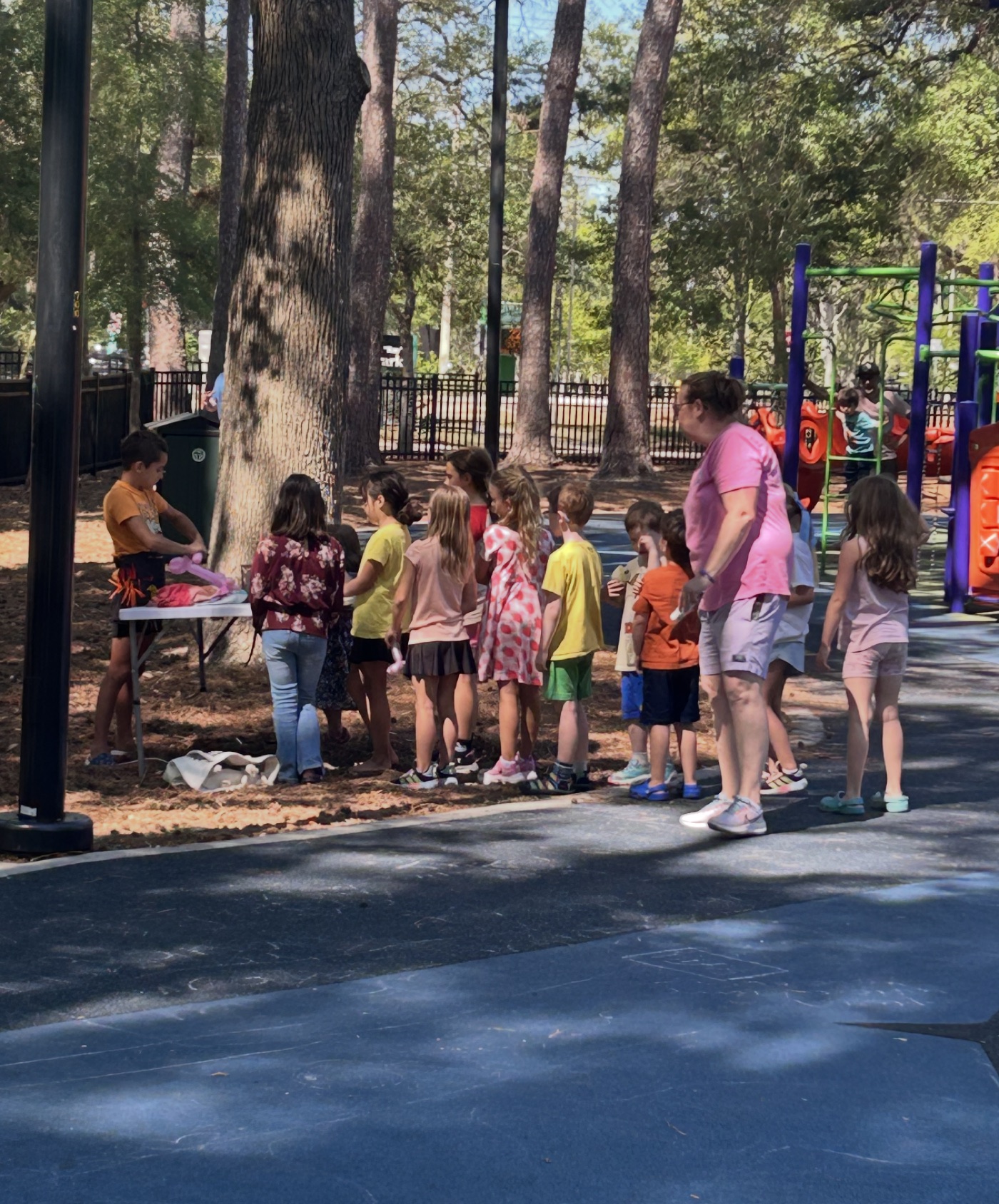 Kids lined up at the park while Leo twists balloons.